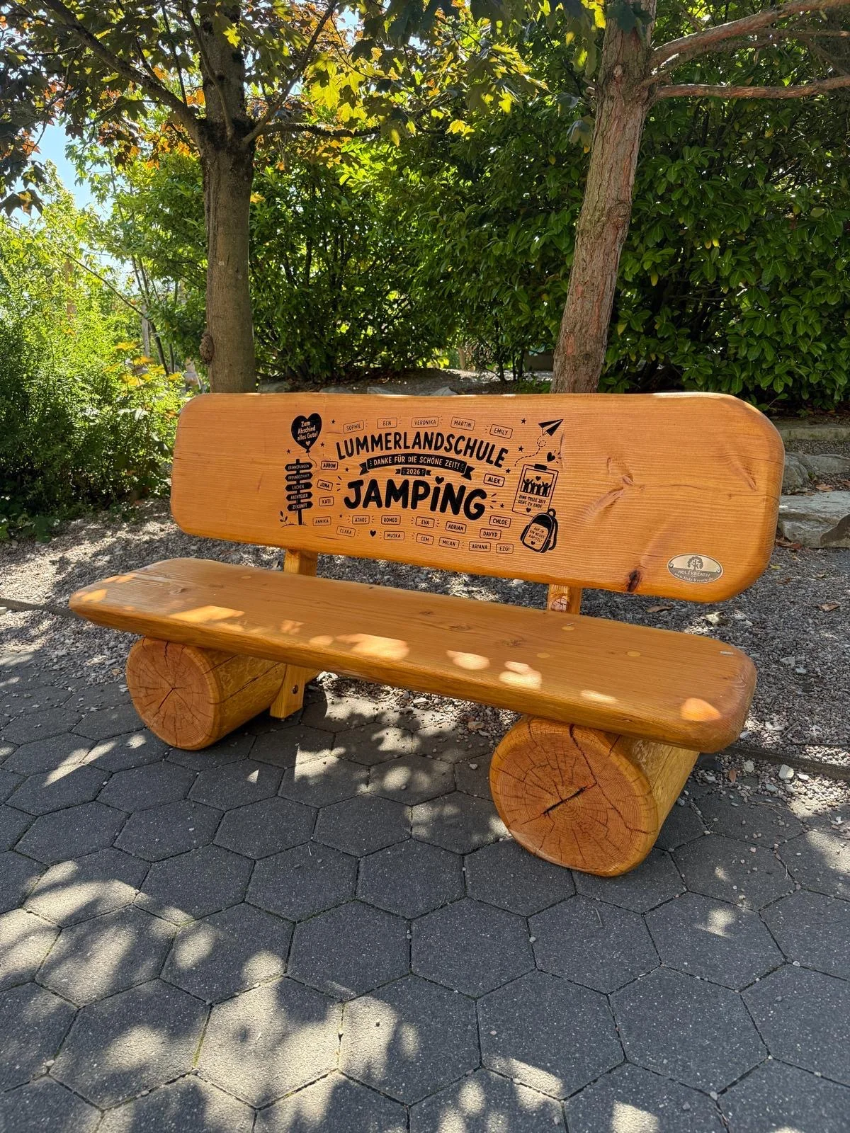 Handgefertigte Sitzbank aus massiver Douglasie mit individueller CNC-Gravur, als Geschenk an die Lehrer der Lummerlandschule auf dem Schulgelände.