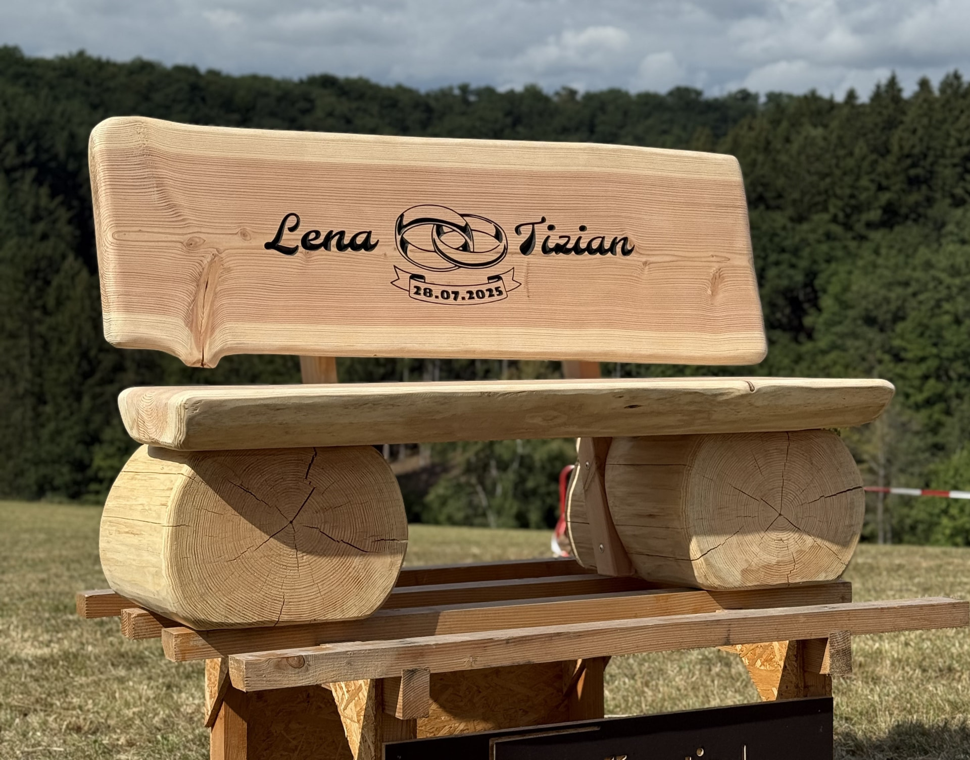 Personalisierte massive Holzbank mit Gravur von Lena und Tizian sowie Datum in natürlicher Außenkulisse