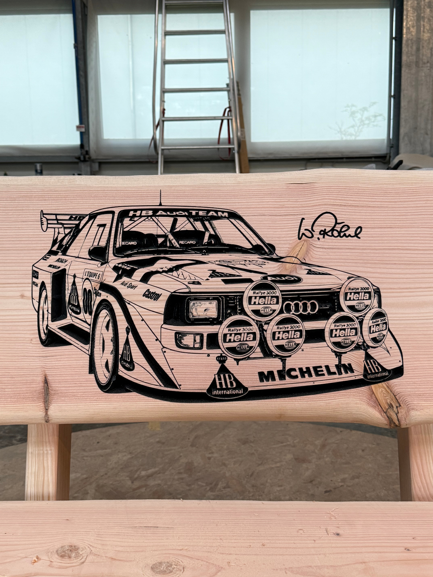 Baumstammbank mit Gravur eines Audi Sport quattro Rallyefahrzeugs und Signatur