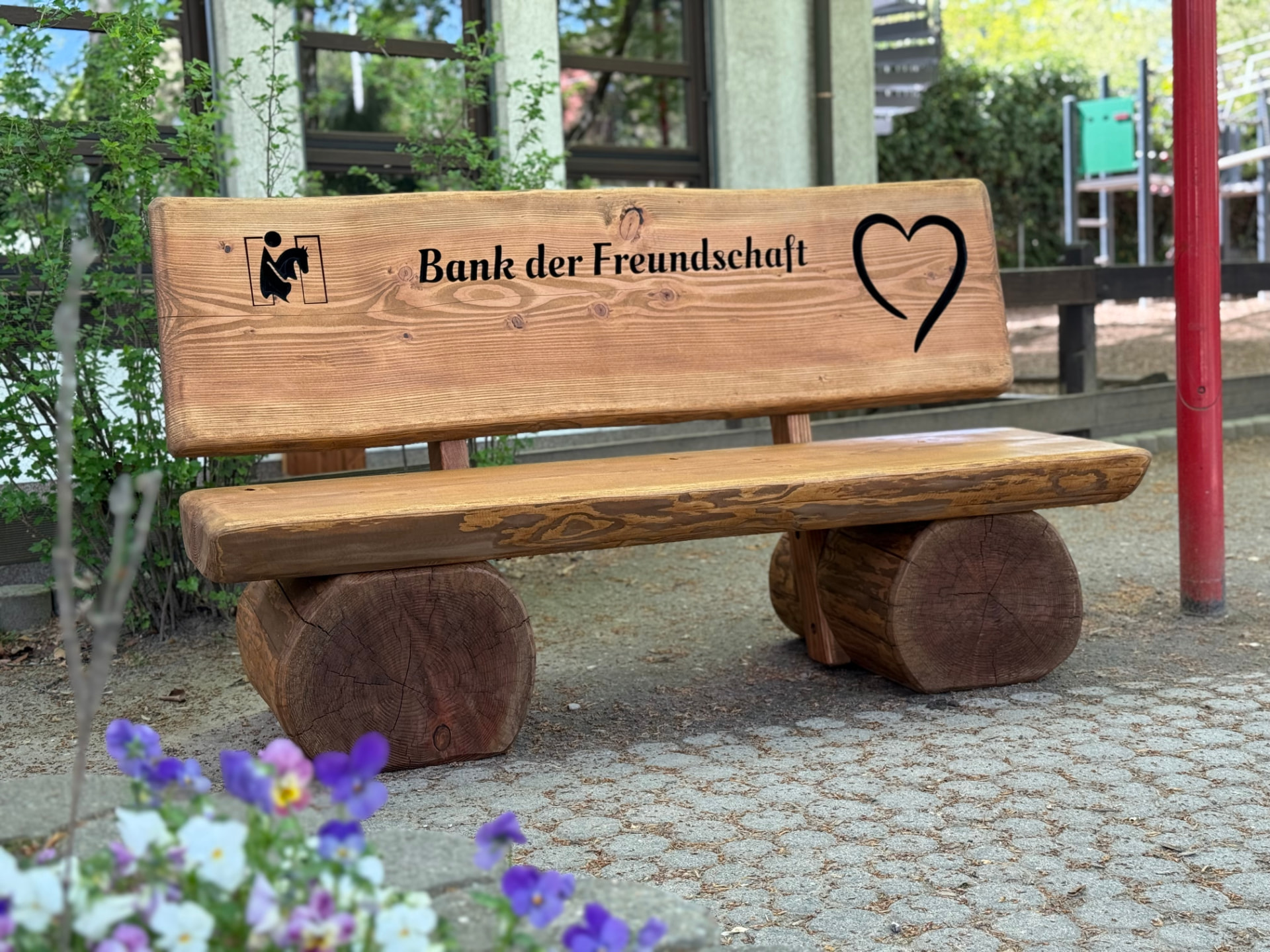 Handgefertigte Freundschaftsbank aus massiver Douglasie mit der Gravur „Bank der Freundschaft“ auf einem Schulhof.