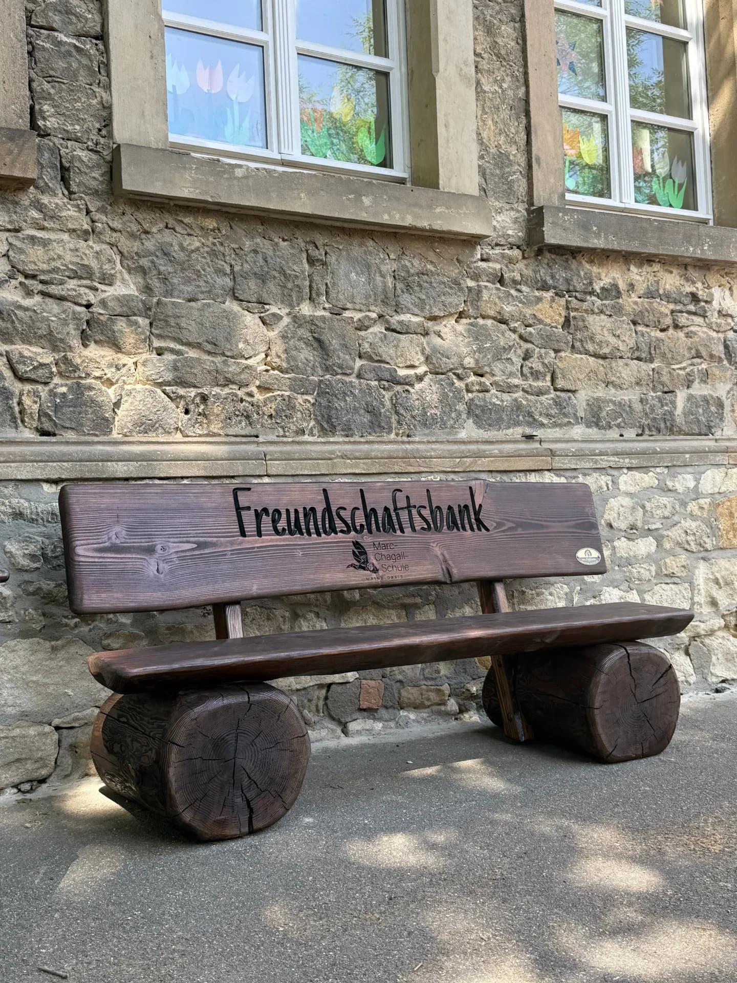 Handgefertigte Freundschaftsbank aus massiver Douglasie mit individueller CNC-Gravur vor der Marc-Chagall-Schule auf dem Schulhof.
