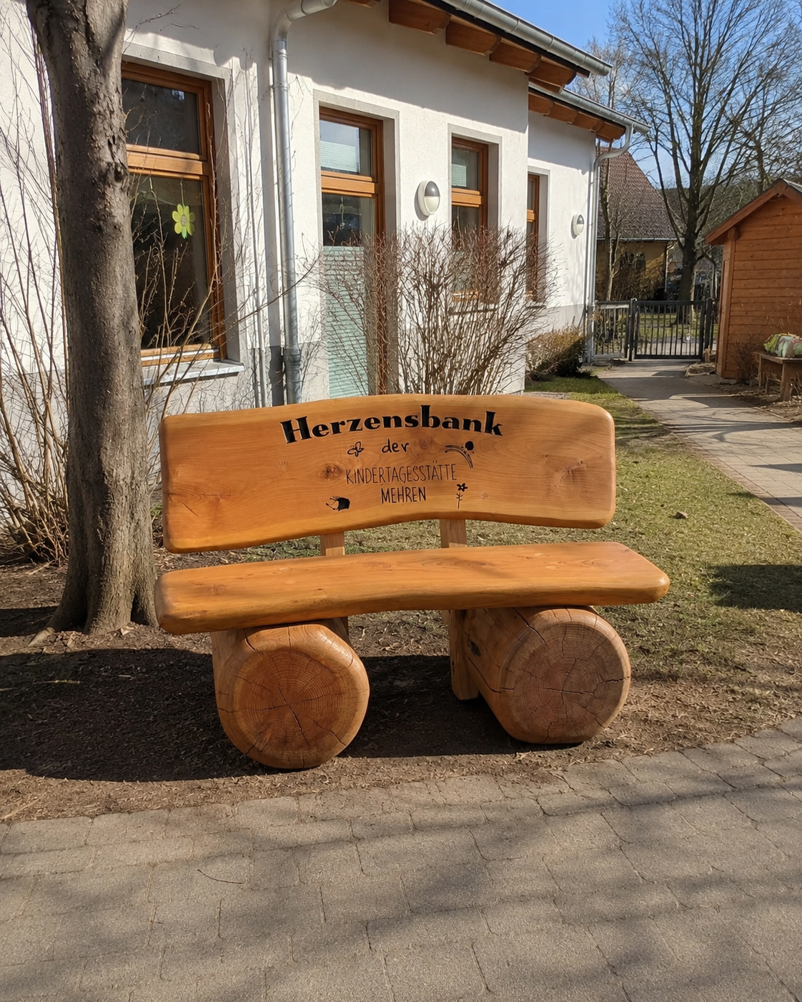 Handgefertigte Herzensbank aus massiver Douglasie mit individueller CNC-Gravur für die Kindertagesstätte Mehren im Außenbereich der Kita.