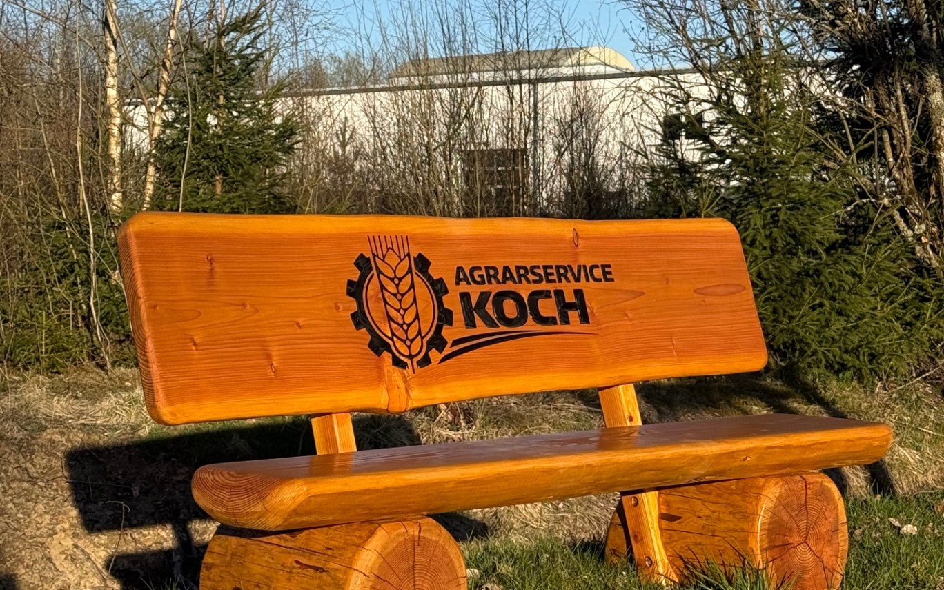 Massive Holzbank mit graviertem Firmenlogo Agrarservice Koch auf dem Firmengelände