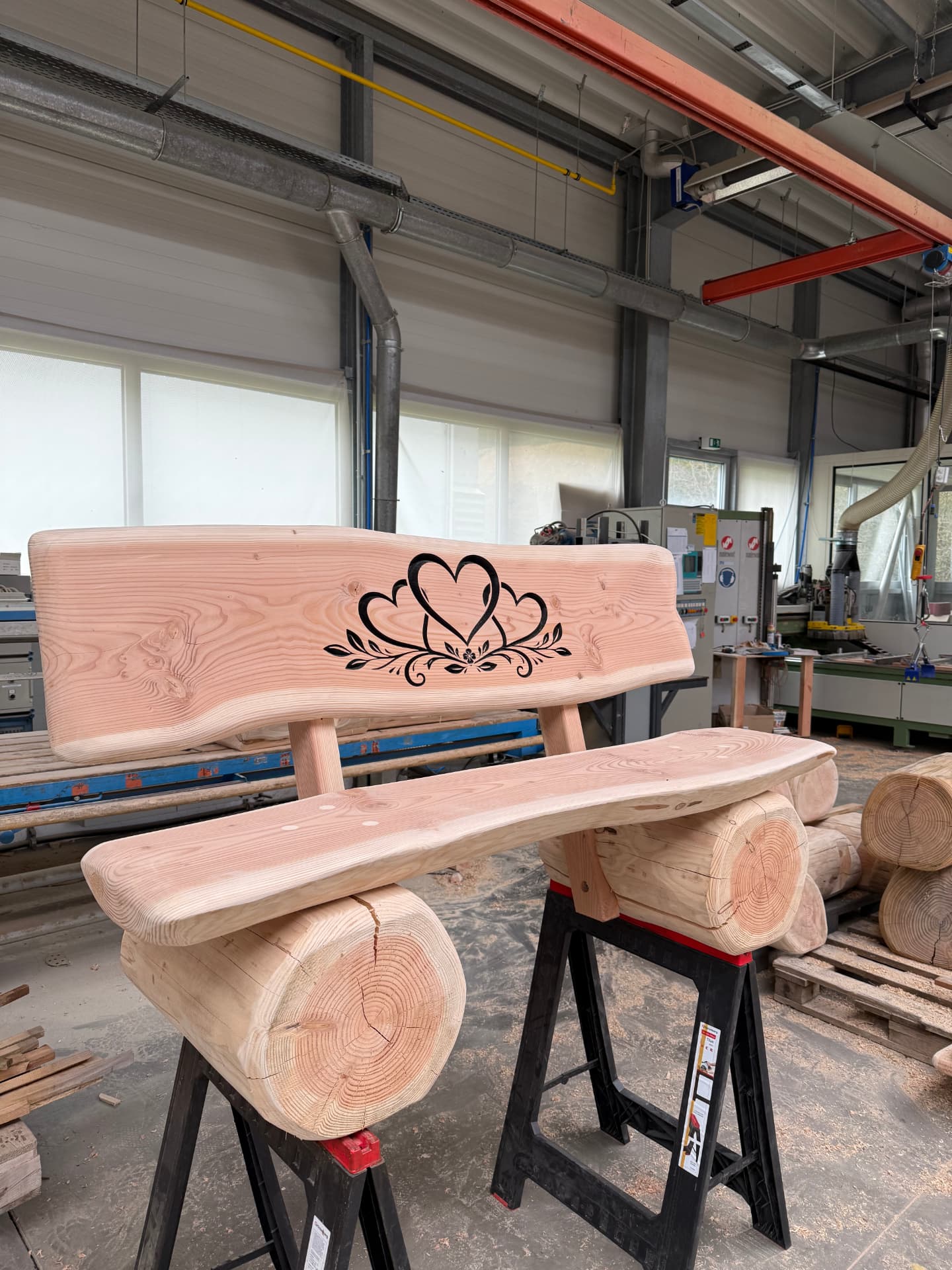 Naturbelassene Baumstammbank mit schwarz ausgearbeiteter CNC-Gravur aus drei Herzen und floralen Ornamenten.
