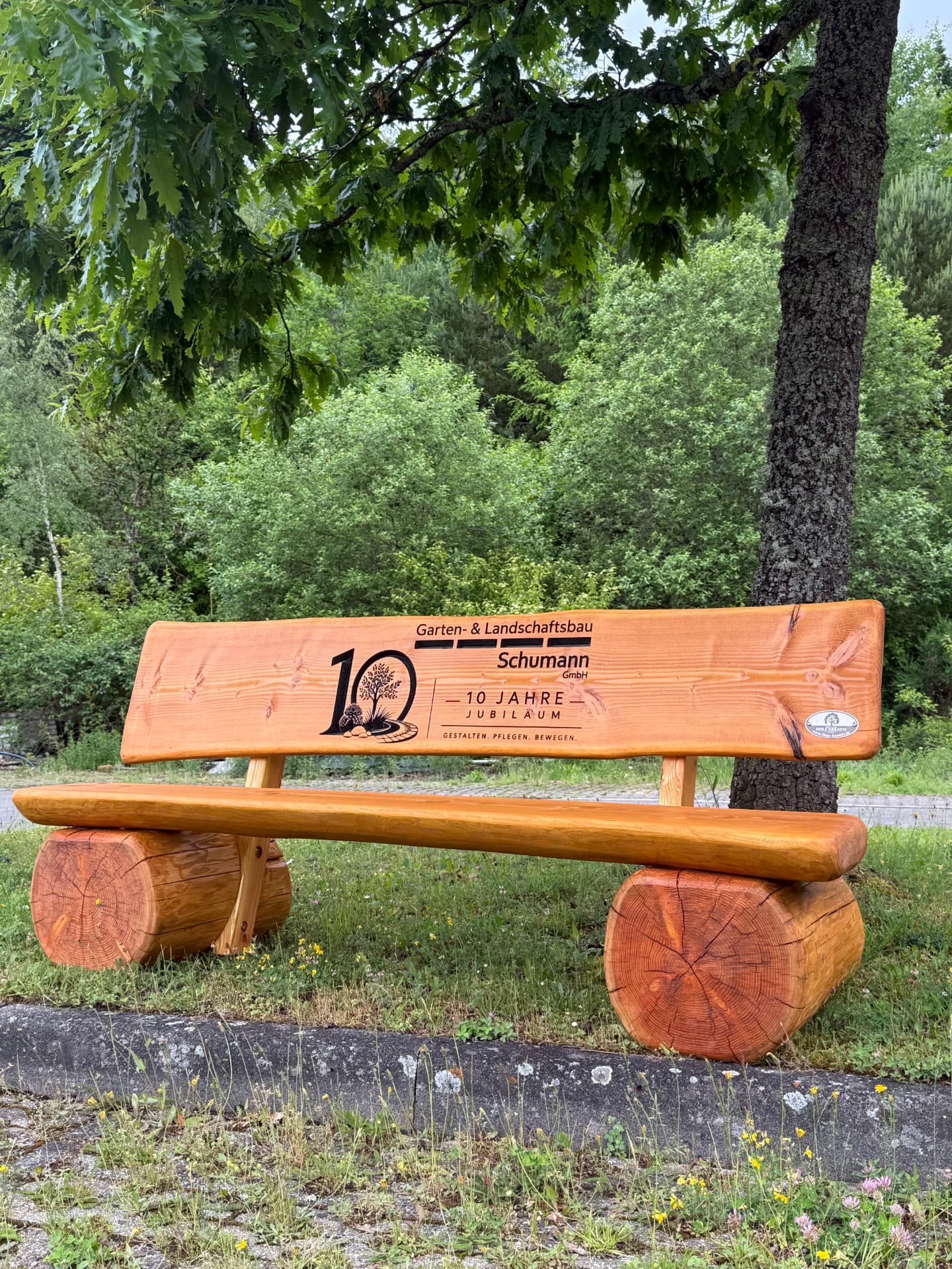 Handgefertigte massive Holzbank mit detailreicher CNC-Gravur zum 10-jährigen Jubiläum von Garten- & Landschaftsbau Schumann GmbH, individuell als repräsentative Firmenbank für das Unternehmen gefertigt.