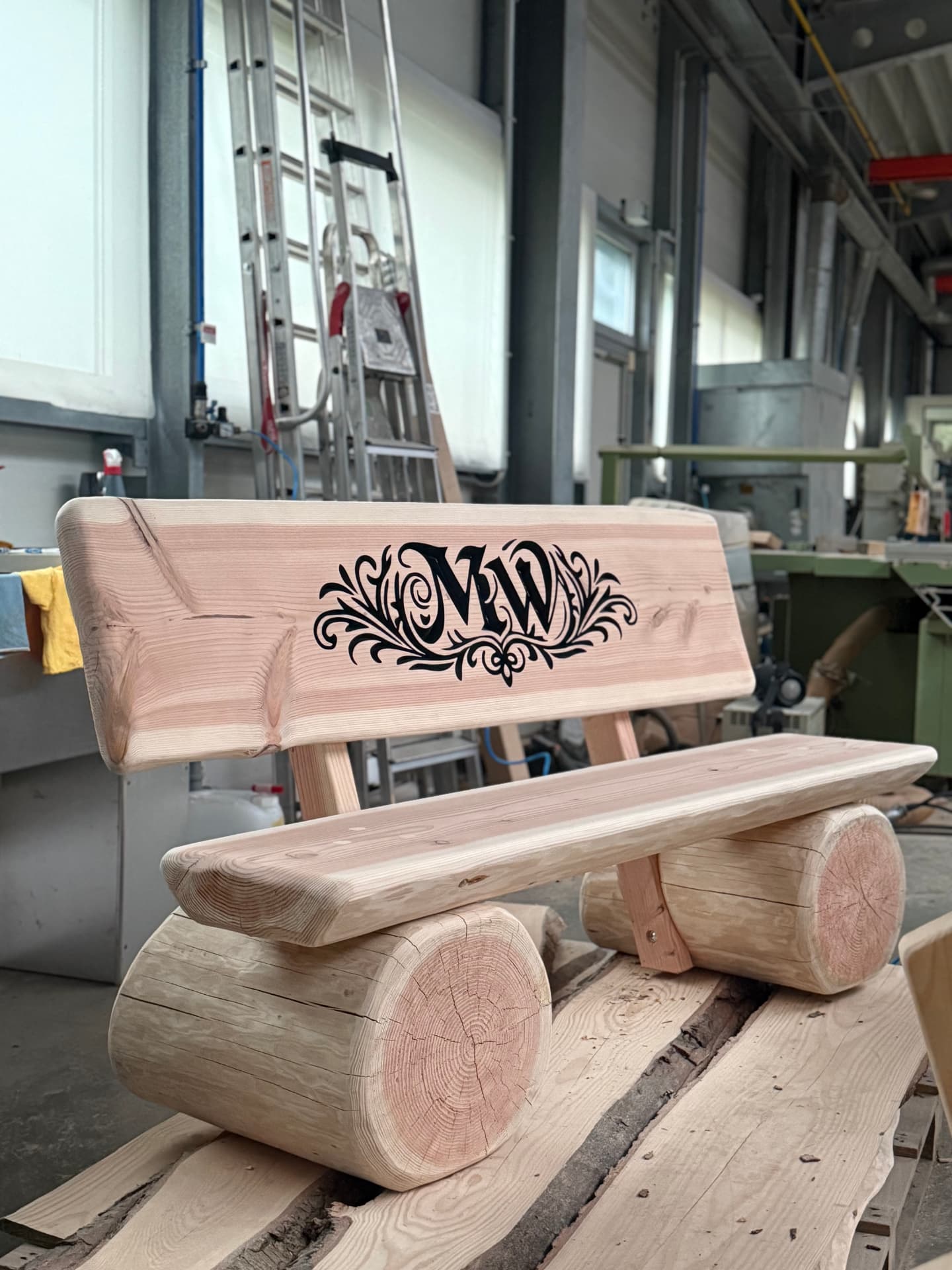 Individuelle Baumstammbank mit schwarz ausgearbeiteter CNC-Gravur des Monogramms MW und floralen Ornamenten.